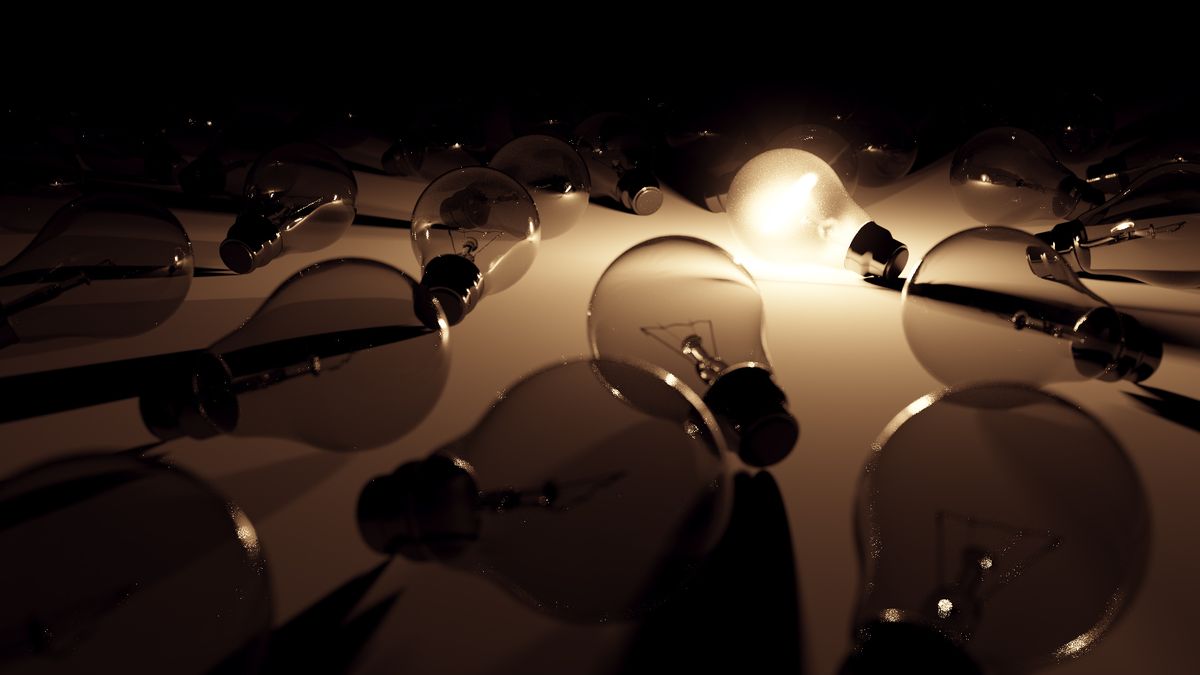Many dark light bulbs, with one lit among them. The light is shining through the glass bodies.